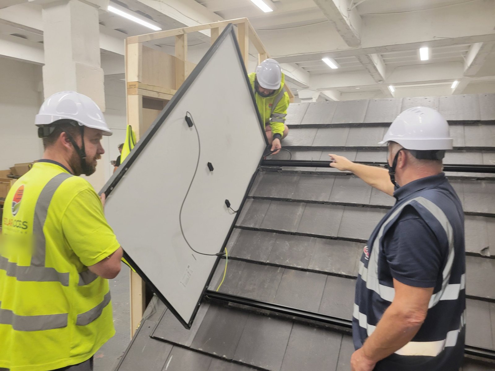 Three installers lifting a solar panel into position on the on-roof mounting rails during training at Cornerstone Vocational Training